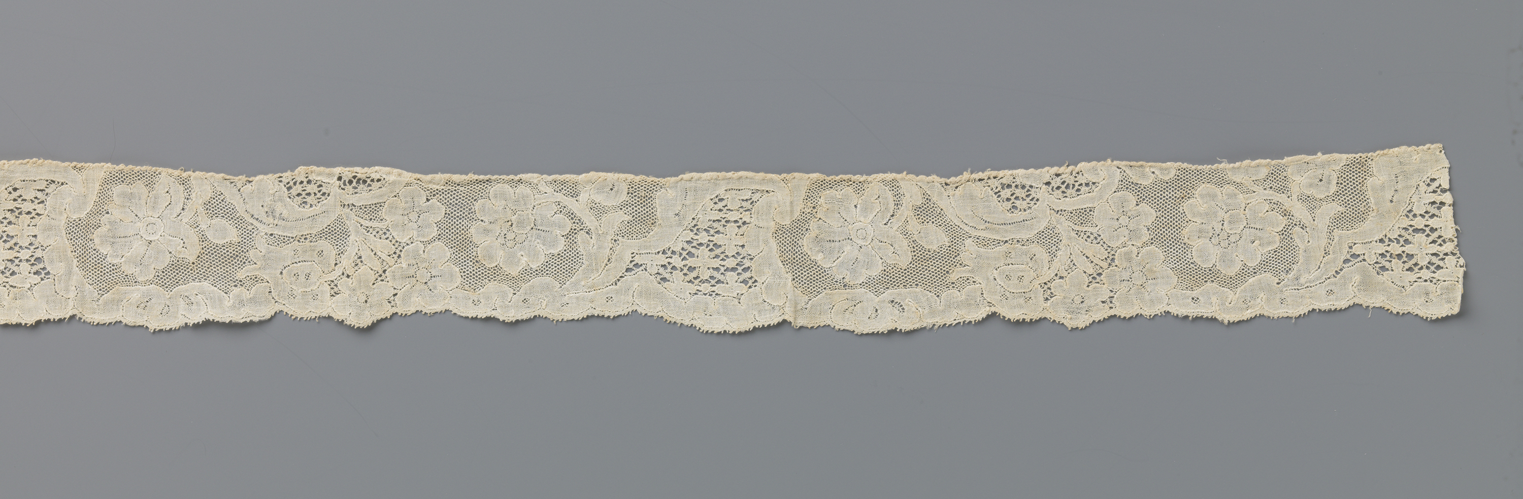 Lace piece by Unknown Artist featuring floral motifs and horn shapes.