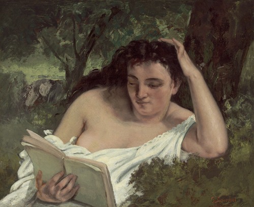 A young woman is sitting in a cozy room, deeply focused on a book she is reading.