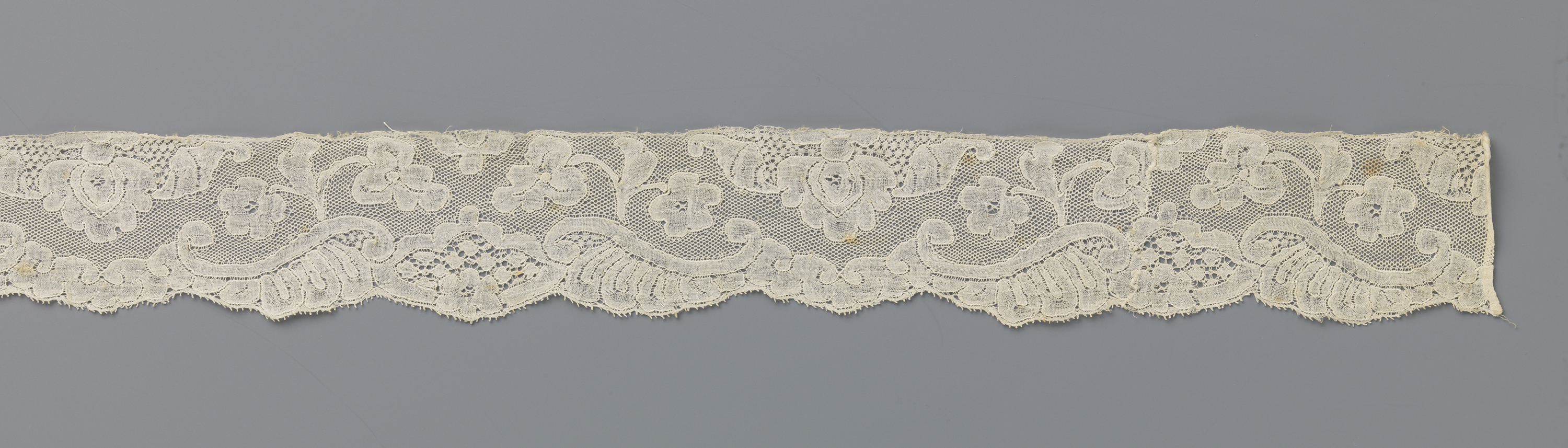 Lace artwork by Unknown Artist featuring a three-lobed cartouche and a dangling flower.