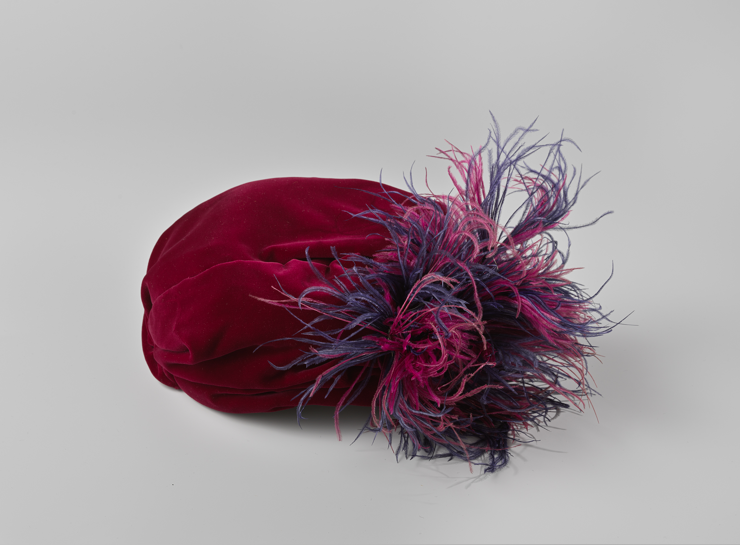 Decorative art piece featuring a dark red velvet hat with feathers by Chapeau Erian