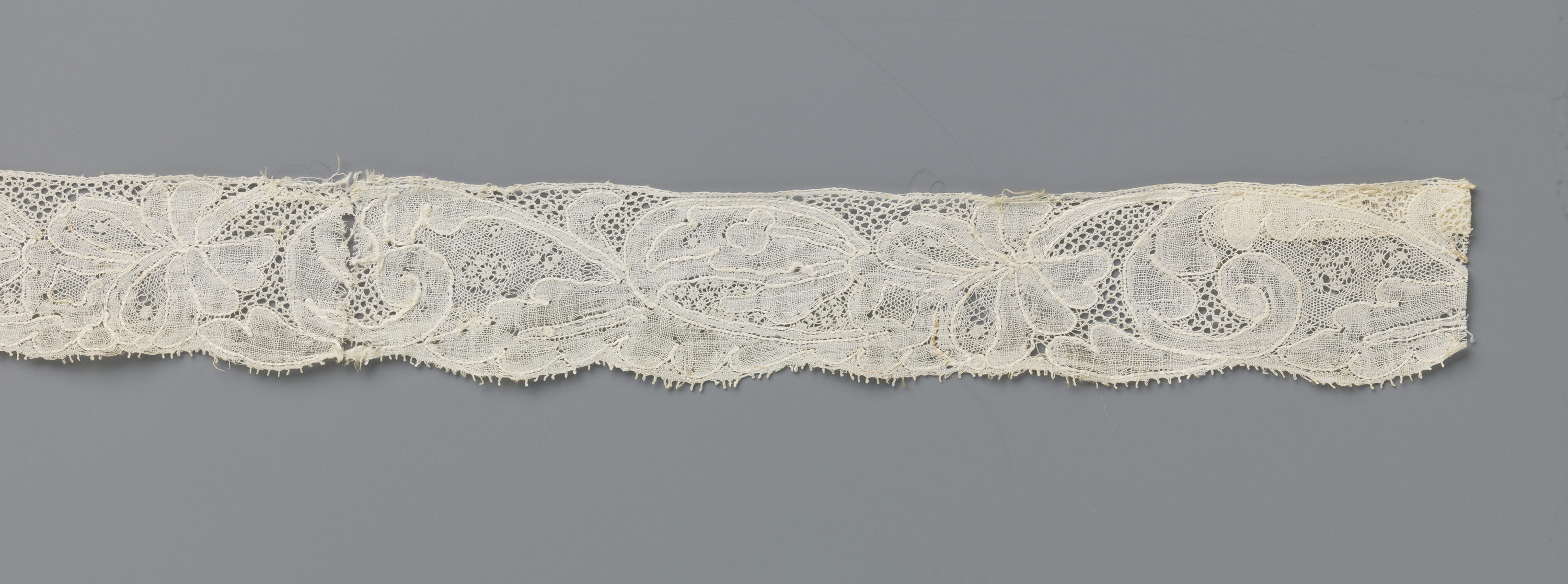 Lace artwork featuring a palmet-shaped flower on a long curved stem by an unknown artist