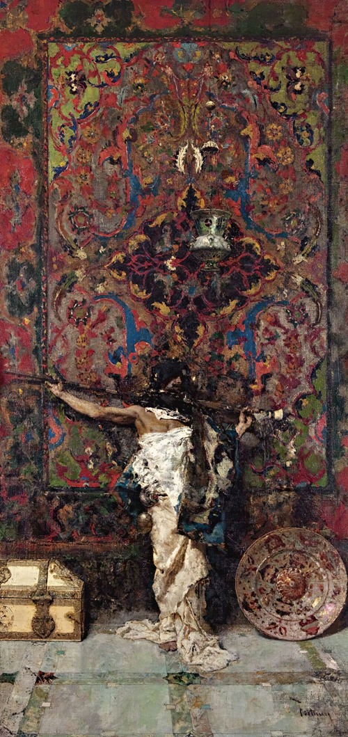 An Arab man stands in traditional attire before a richly decorated tapestry.