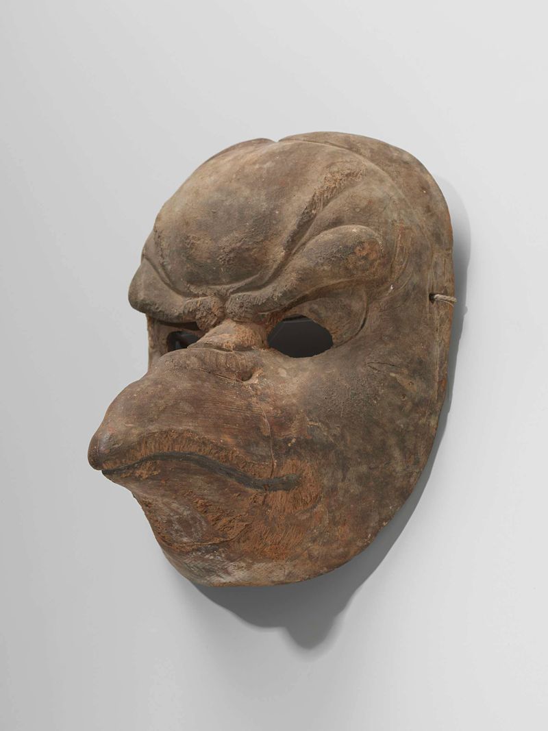 Escultura figurativa em madeira de um rosto mascarado por Artista Desconhecido